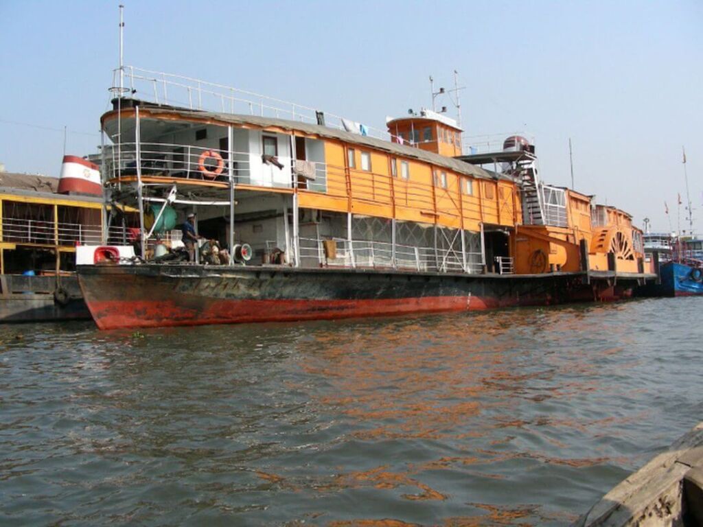 An orange paddle steamer sits on the water next to other boats.