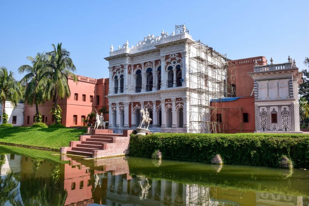 A stunning palace complex with intricate designs, statues, scaffolding, and reflective water in Dhaka, Bangladesh.