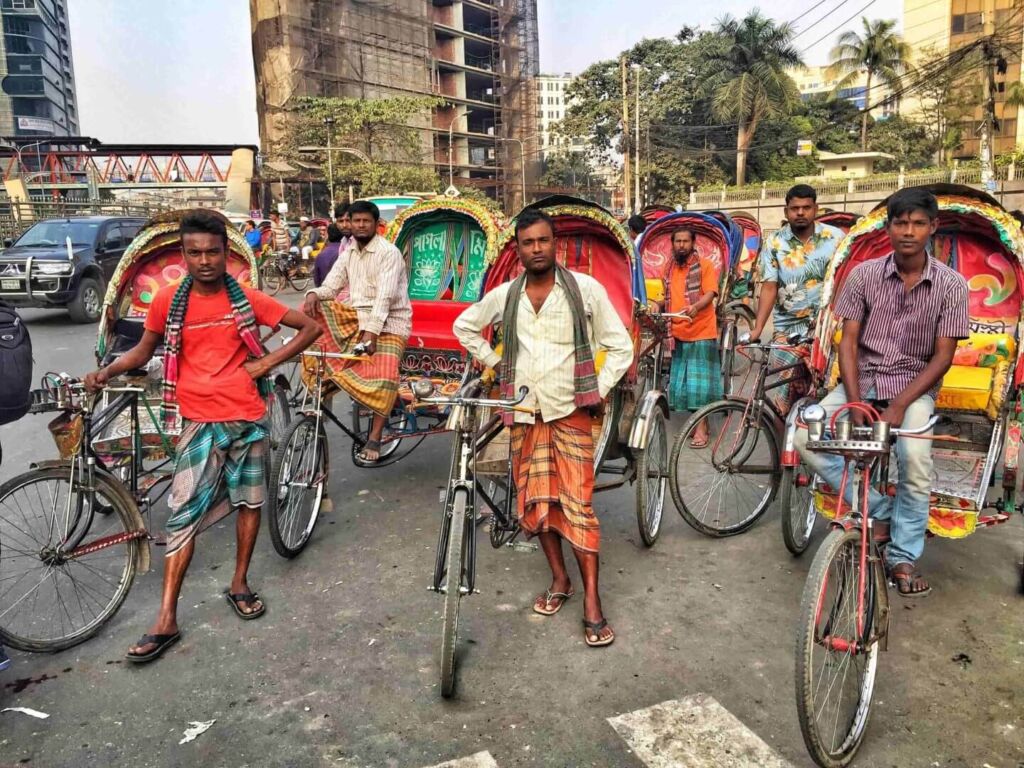 A group of men stand with their rickshaws on a street in Bangladesh, posing for a picture.