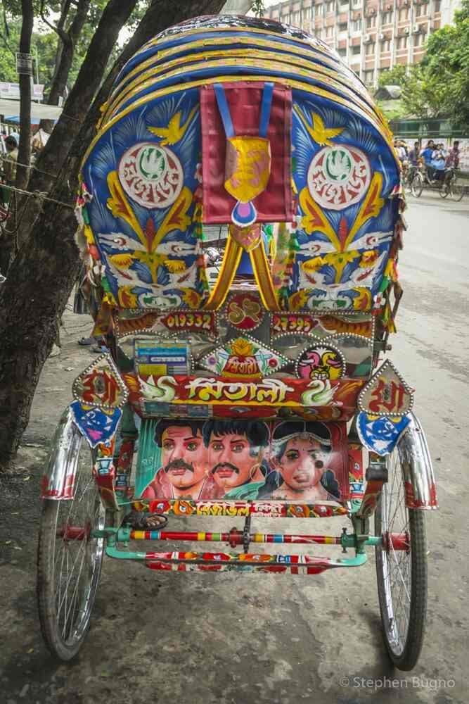 A brightly decorated rickshaw in Bangladesh with colorful designs, portraits, and license plates.