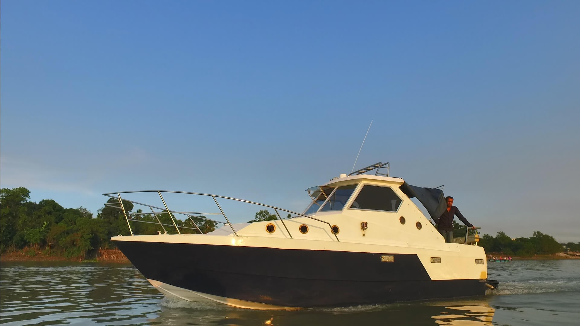 A motorboat with a person on board is gliding on the water with trees visible in the background under a clear blue sky.