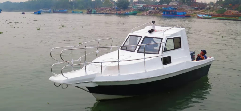 A white and black boat with a man relaxing on the back floats on a calm river with other boats in the background.