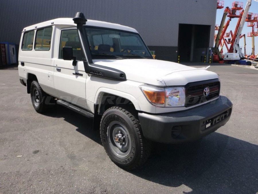A white Toyota Land Cruiser 70 Series parked on a concrete lot in front of an industrial building and red scissor lifts.