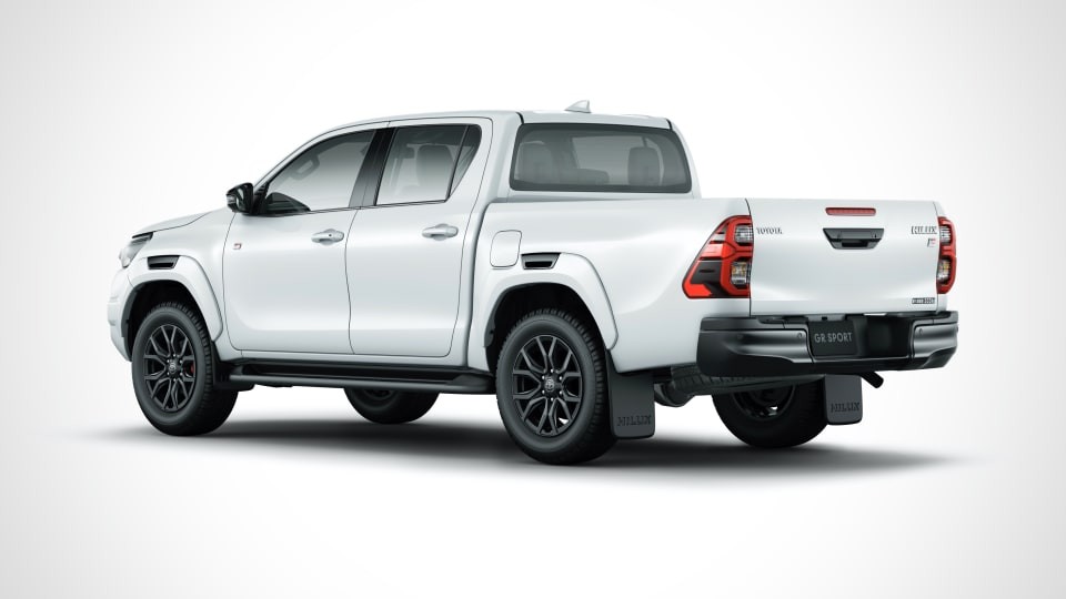 A white Toyota Hilux GR Sport pickup truck is viewed from the rear three-quarter angle, highlighting its black wheels, black rear bumper, and overall rugged yet sporty design.