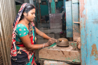 Pottery Workshop A woman in a colorful sari is working with clay on a pottery wheel, using a tool to shape a bowl.