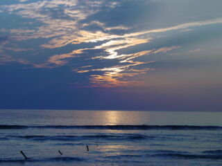 A scenic view of the ocean at sunset, with a dramatic sky and calm waters.