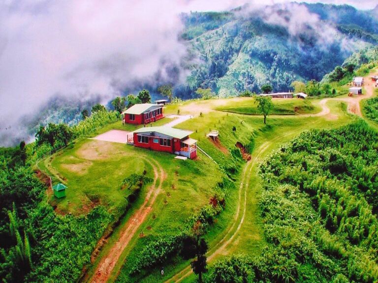A scenic view of houses on a green hillside with fog and mountains in the background.