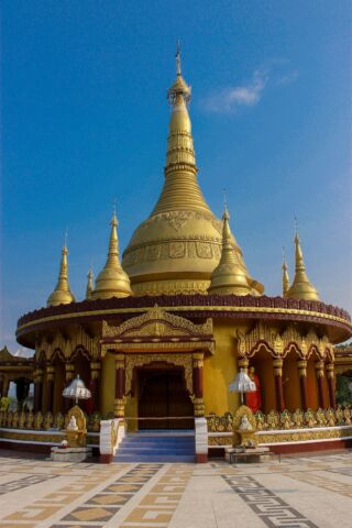 A golden Buddhist temple with ornate details stands tall against a clear blue sky.