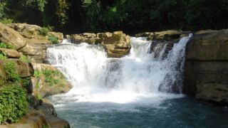 Nafakhum Waterfall A beautiful waterfall cascading over rocky ledges into a pool of turquoise water, surrounded by lush green vegetation.