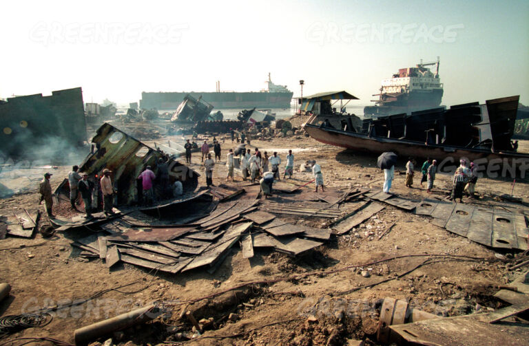 This photo shows a ship breaking yard with workers dismantling ships amidst piles of metal debris, highlighting the hazardous conditions and environmental concerns.