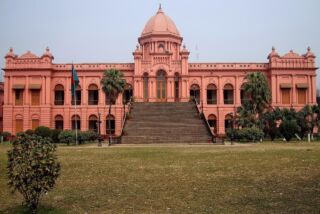 Bangladesh Visa on Arrival for Chinese Citizens: Complete Guide A pink palace with a large staircase in front of a grassy lawn is depicted in a symmetrical, eye-level shot.