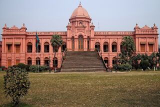 Dhaka Full-Day Tour with Visa-on-Arrival Assistance A grand, pink-colored building with a large staircase leading up to its entrance, set against a clear sky and a sprawling lawn.