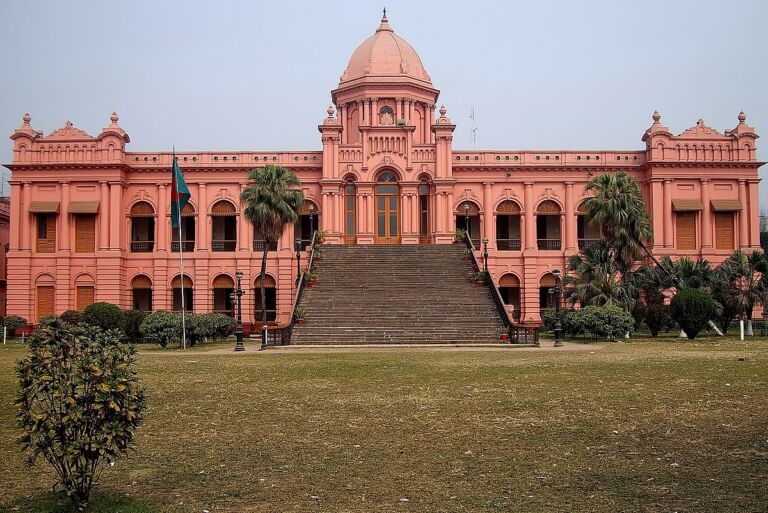 A grand, pink-colored building with a large staircase leading up to its entrance, set against a clear sky and a sprawling lawn.