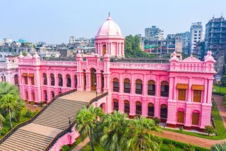 Bangladesh VISA on Arrival Invitation Letter This eye-level shot features a vibrant pink building with a dome, accessible by a grand staircase, surrounded by lush greenery.